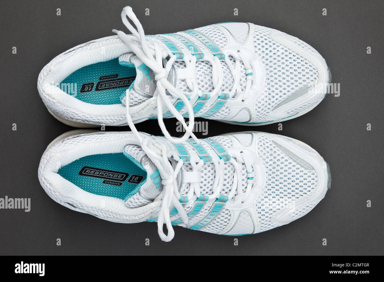 A pair of women's new white and blue Adidas air cushion trainers sneakers with laces tied on a dark grey background from overhead. England UK Britain Stock Photo