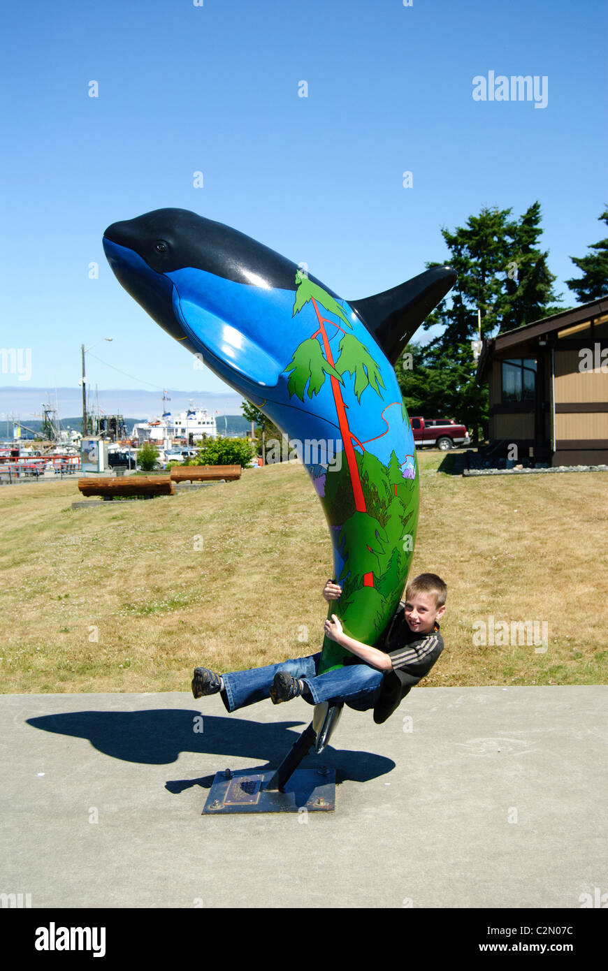 Boy playing on orca (killer whale) statue, Port McNeill, Vancouver Island, British Columbia, Canada Stock Photo