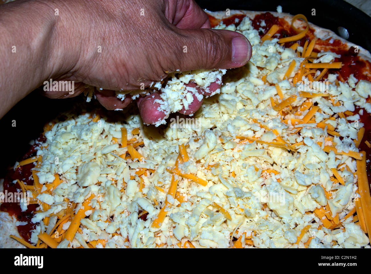 Sprinkling grated cheddar mozarella cheese rich tomato sauce on pizza