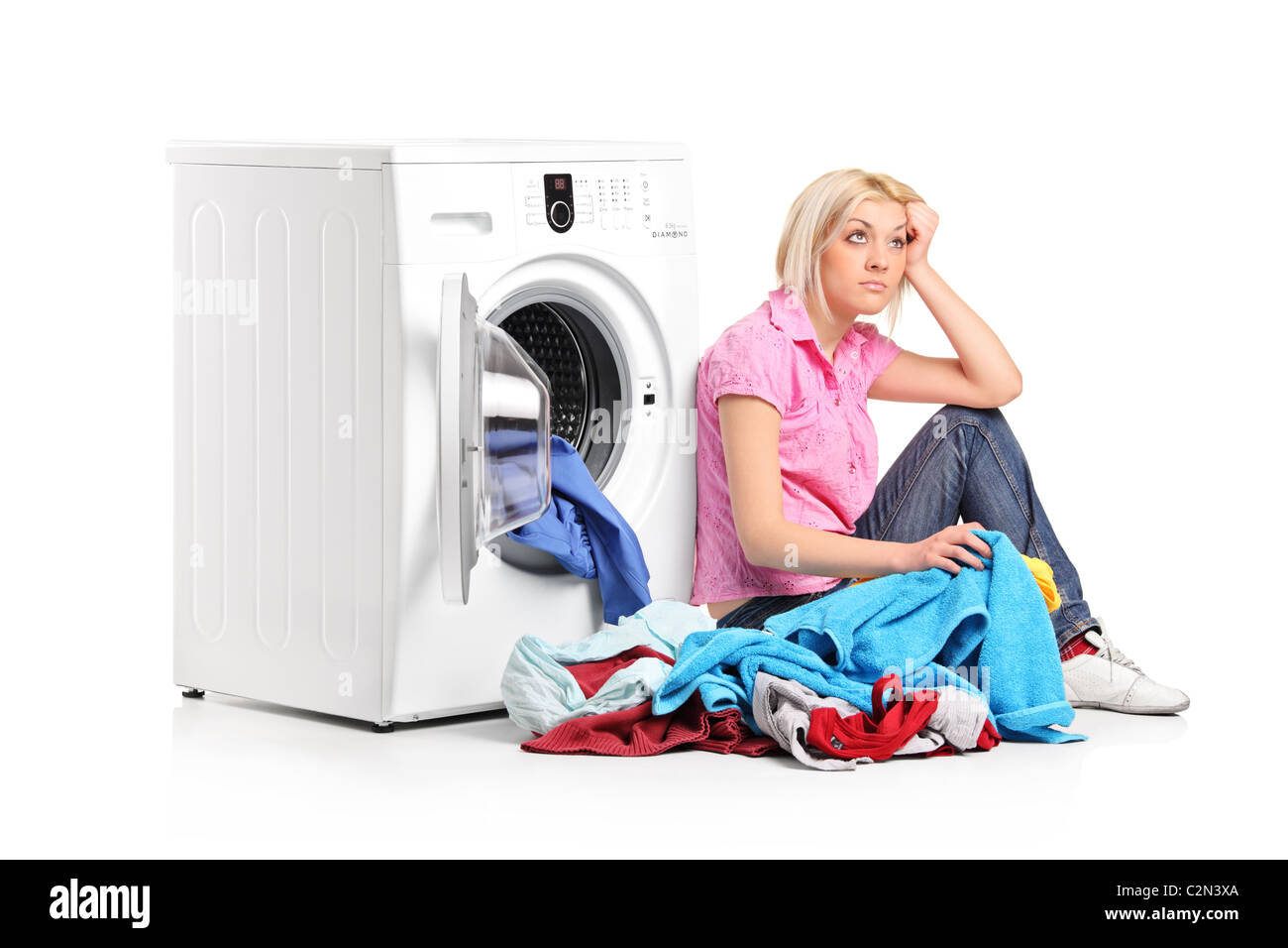A thoughtful young woman with clothes seated next to a washing machine Stock Photo