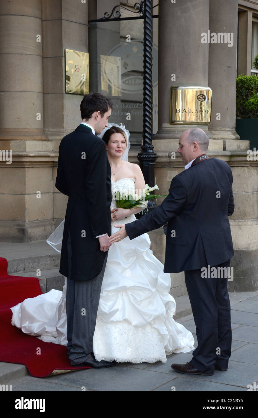 A wedding photographer poses the bride and groom outside the Balmoral Hotel on Princes Street, Edinburgh. Stock Photo