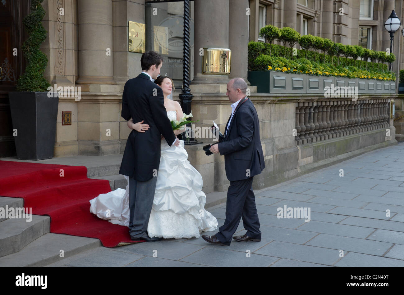 A wedding photographer poses the bride and groom outside the Balmoral Hotel on Princes Street, Edinburgh. Stock Photo