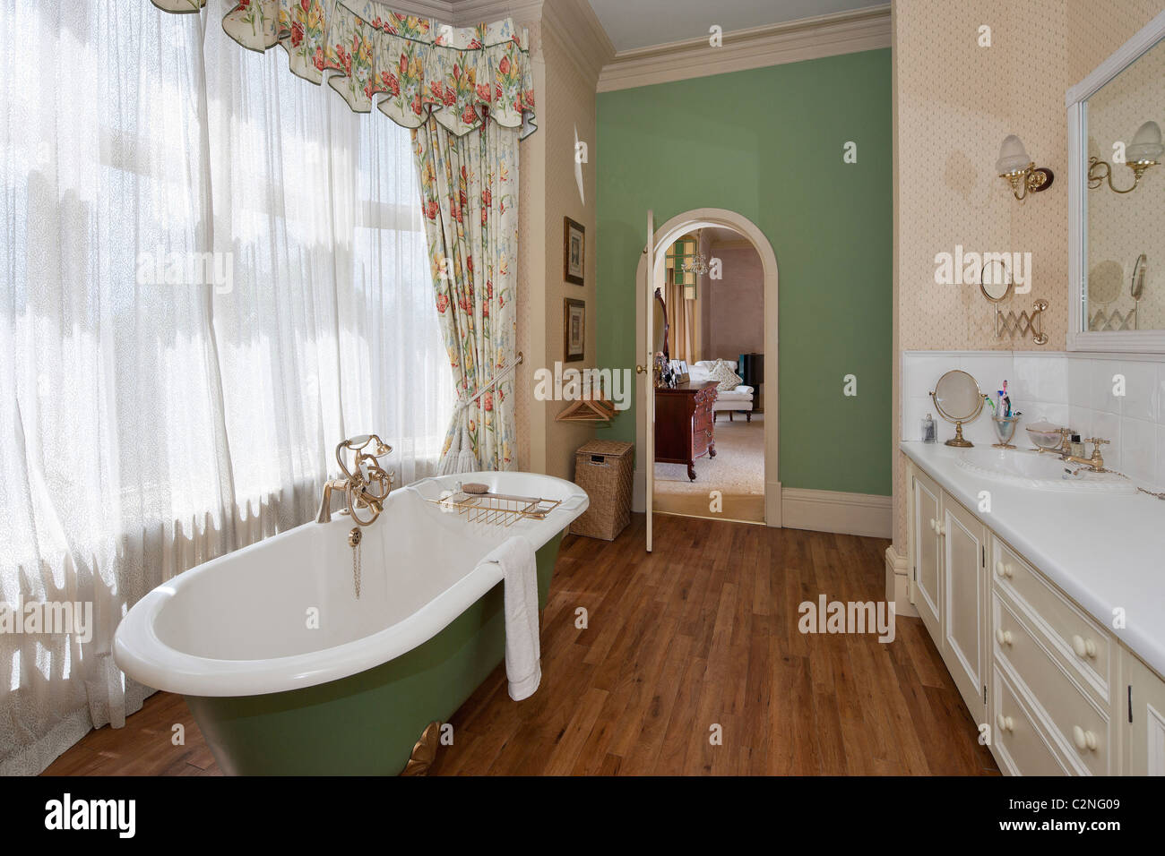 Ensuite bathroom with roll top bath, wooden floor an window drapes Stock Photo
