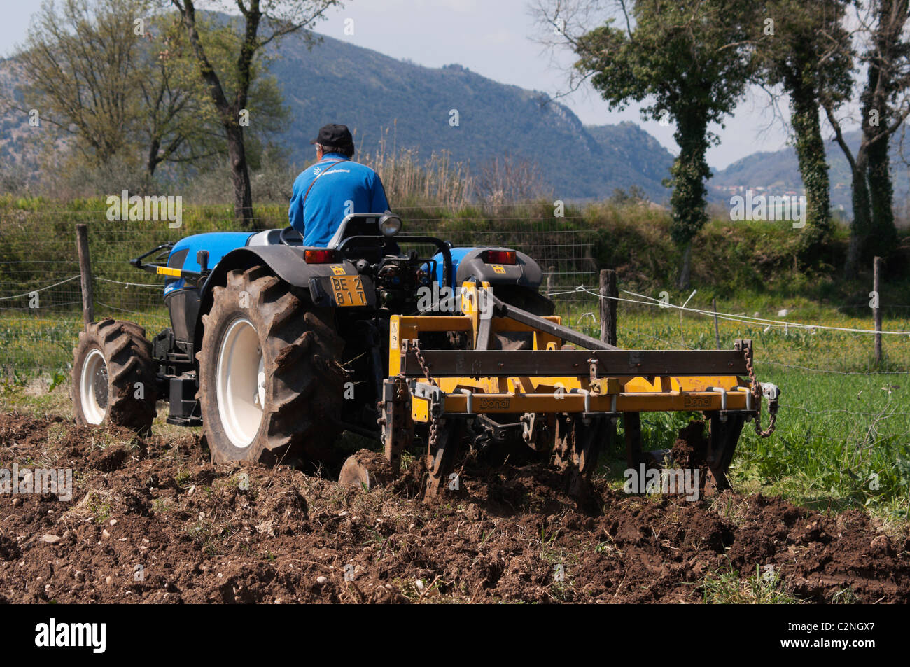 Contemporary farmer driving a tractor on ploughed land on a small farm in Italy, with ripper tool to remove weeds. Stock Photo