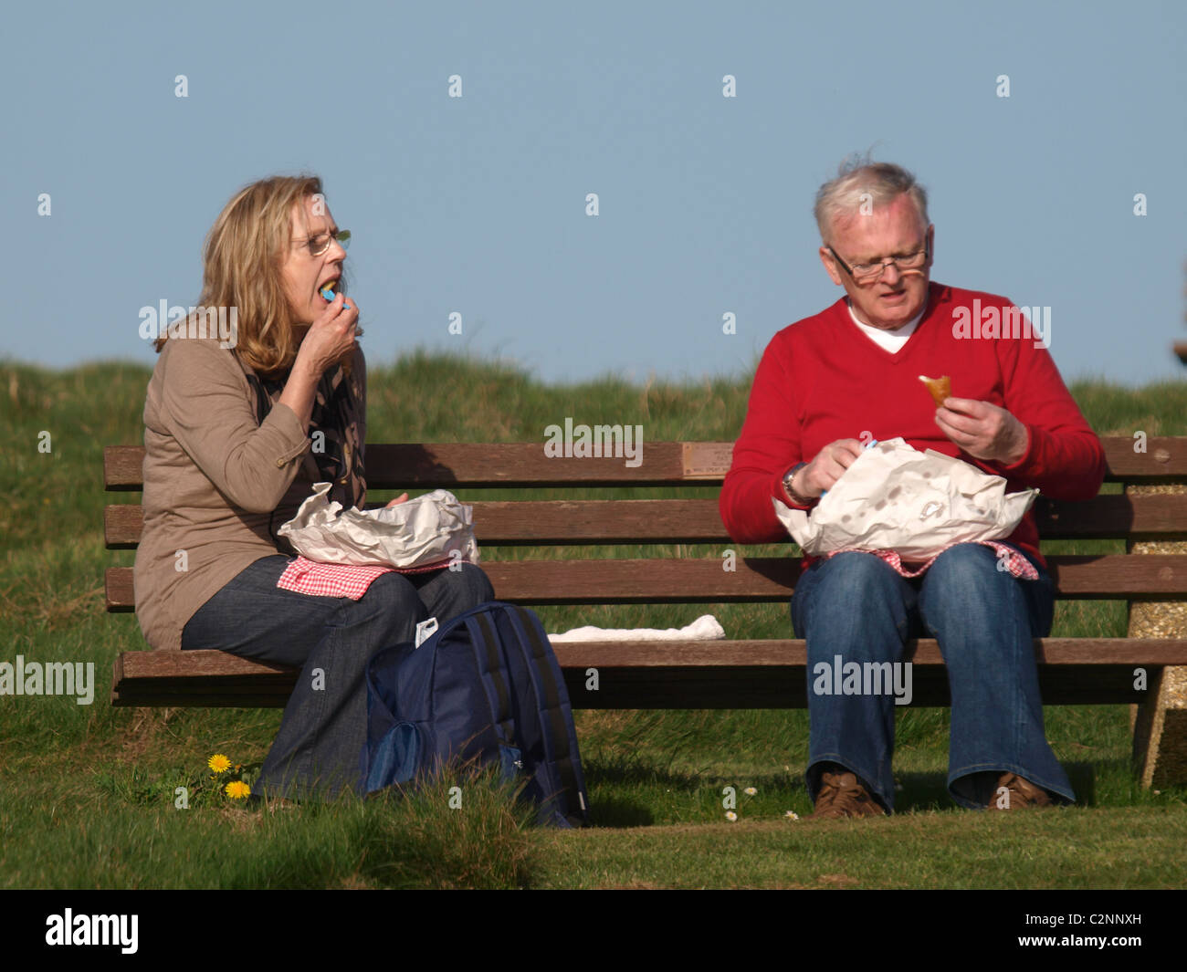 Old couple sat on a bench eating fish and chips, Cornwall, UK Stock Photo