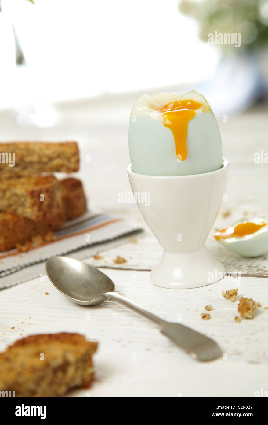 Soft boiled egg with bread toast spoon in bright contemporary setting spoon dripping yolk Stock Photo