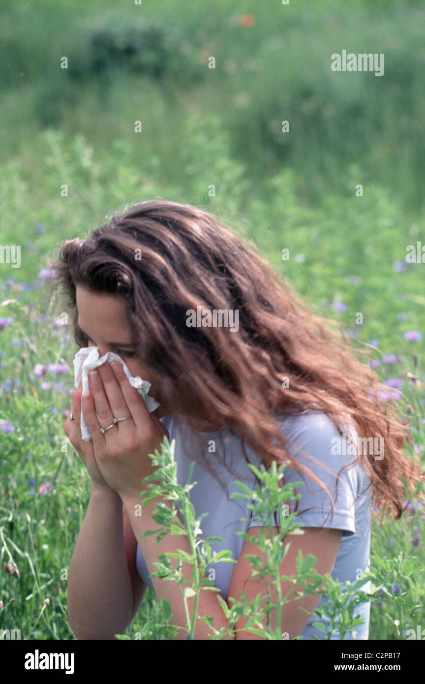Young Caucasian woman sneezing in hankie, suffering from pollen hay fever in a flower field outside  SerieCVS100019 Stock Photo