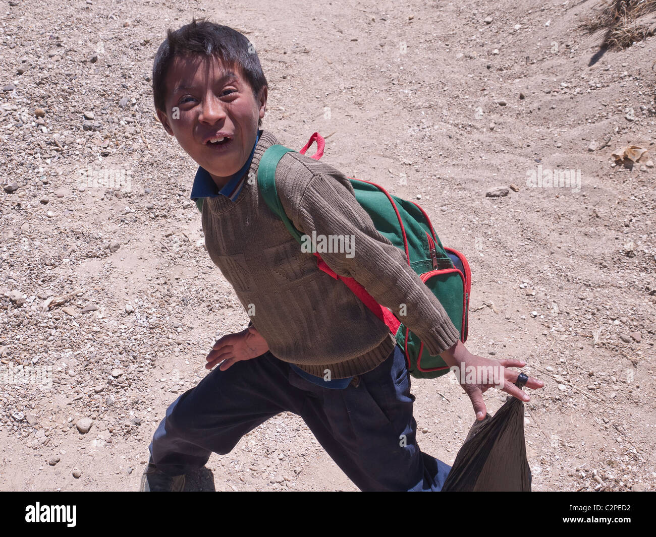 A primary school boy makes a very funny face as he runs across the dirt  road in Totonicapan, Guatemala Stock Photo - Alamy