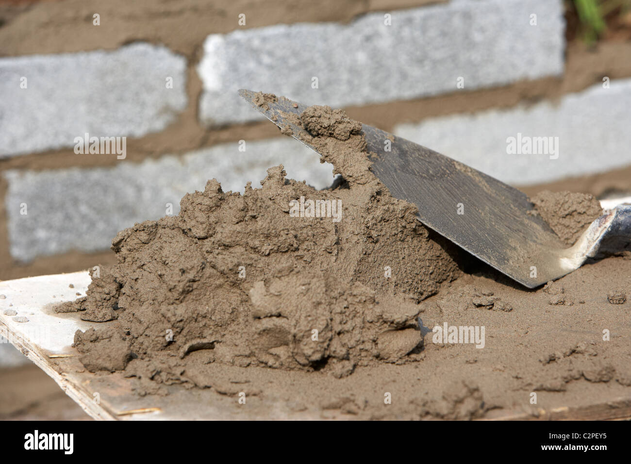 bricklaying trowel and mortar piled up on a wooden board ready for building a block retaining wall in the uk Stock Photo