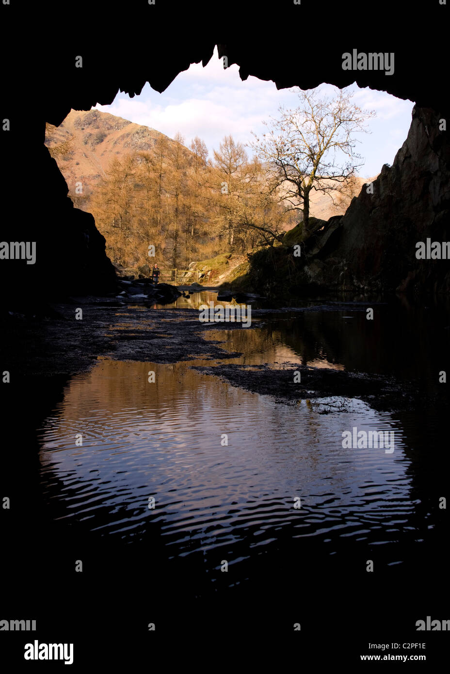 Silhouette of Rydal cave entrance with reflection of sunlit Lakeland fells opposite, Rydal, Lake District, Cumbria, UK Stock Photo