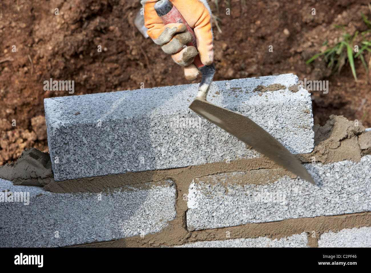 bricklayer building a wall (motion blur on hand) with half cement breeze blocks building a block retaining wall in the uk Stock Photo