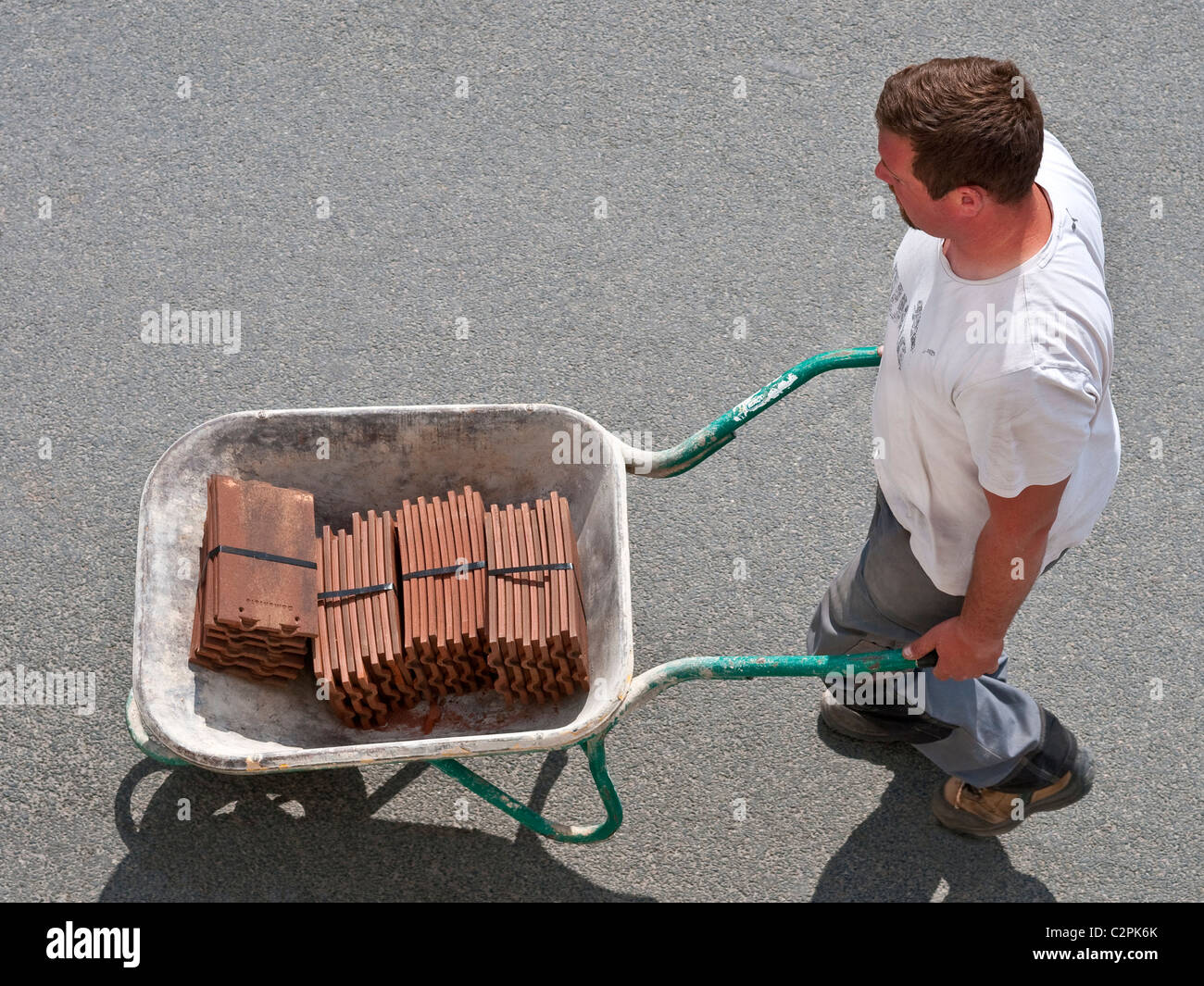 Workman walking along street with wheelbarrow carrying new roofing tiles - France. Stock Photo