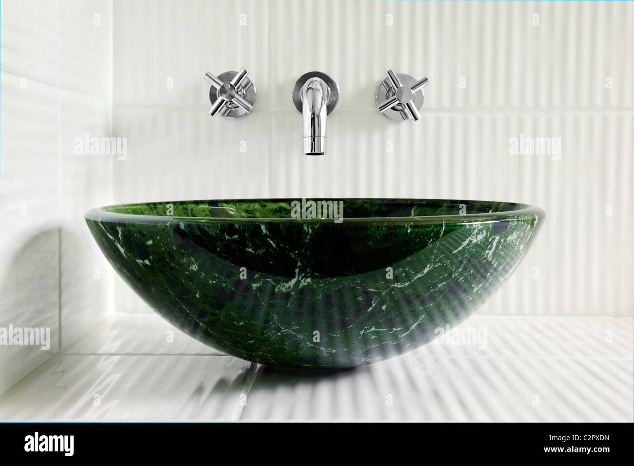 Modern style green marble vessel sink with wall mount faucets on bright white corrugated tiles. Stock Photo