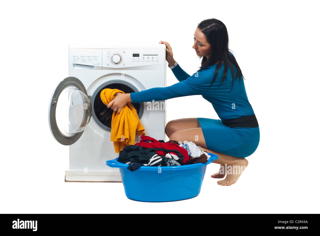 Young housewife in blue dress loading washing machine isolated on white