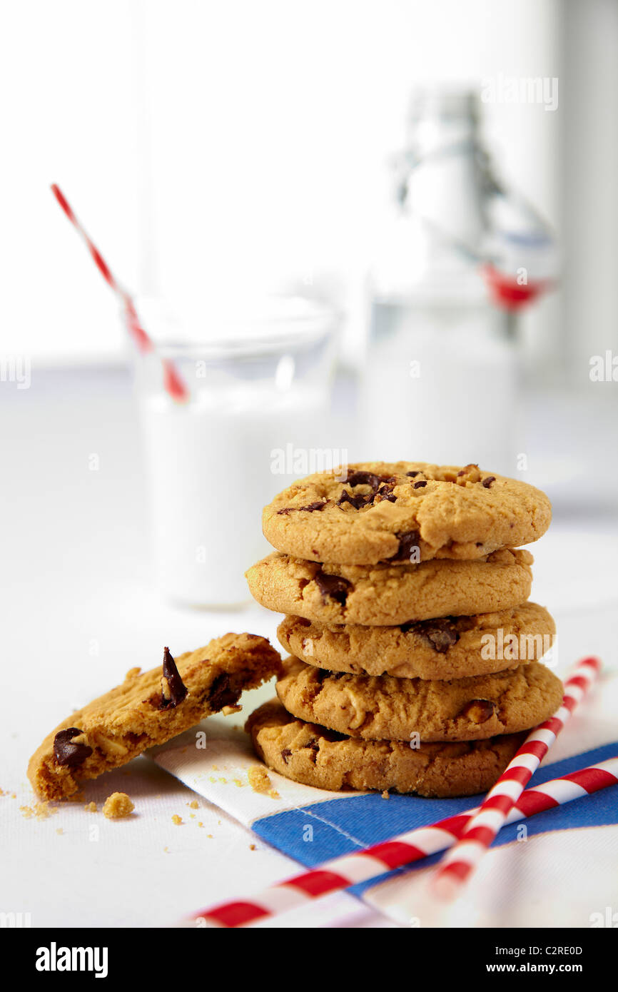 Stack of chocolate chip cookies with red strip drinking straws. Milk in