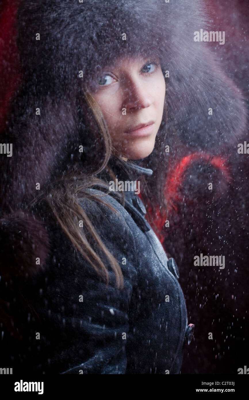 A young girl wearing a fur winter hat looking through falling snow Stock Photo