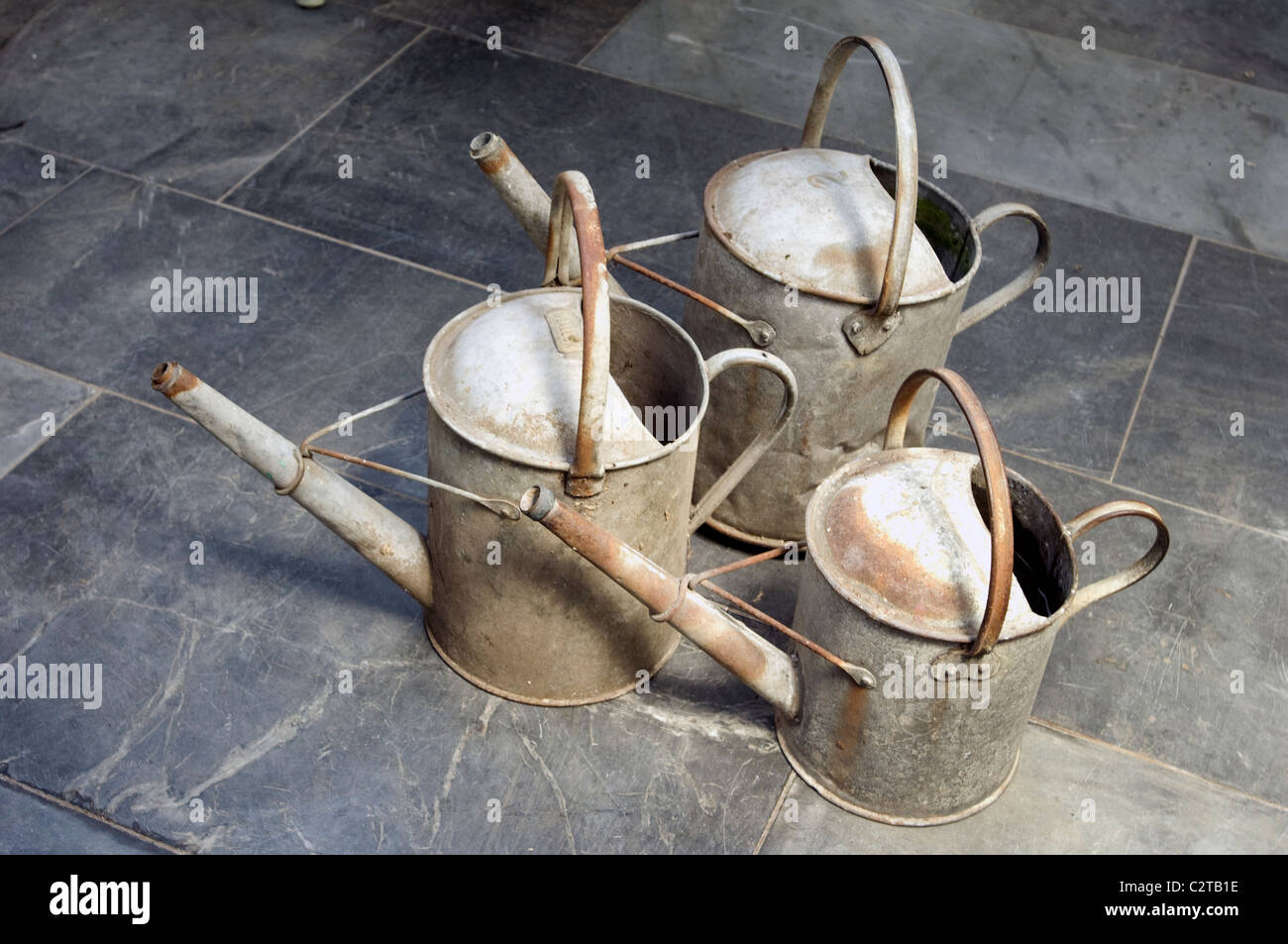 Old 1-gallon, 11/2 gallon and 2 gallon galvanised iron watering cans on a slate floor in a greenhouse Stock Photo