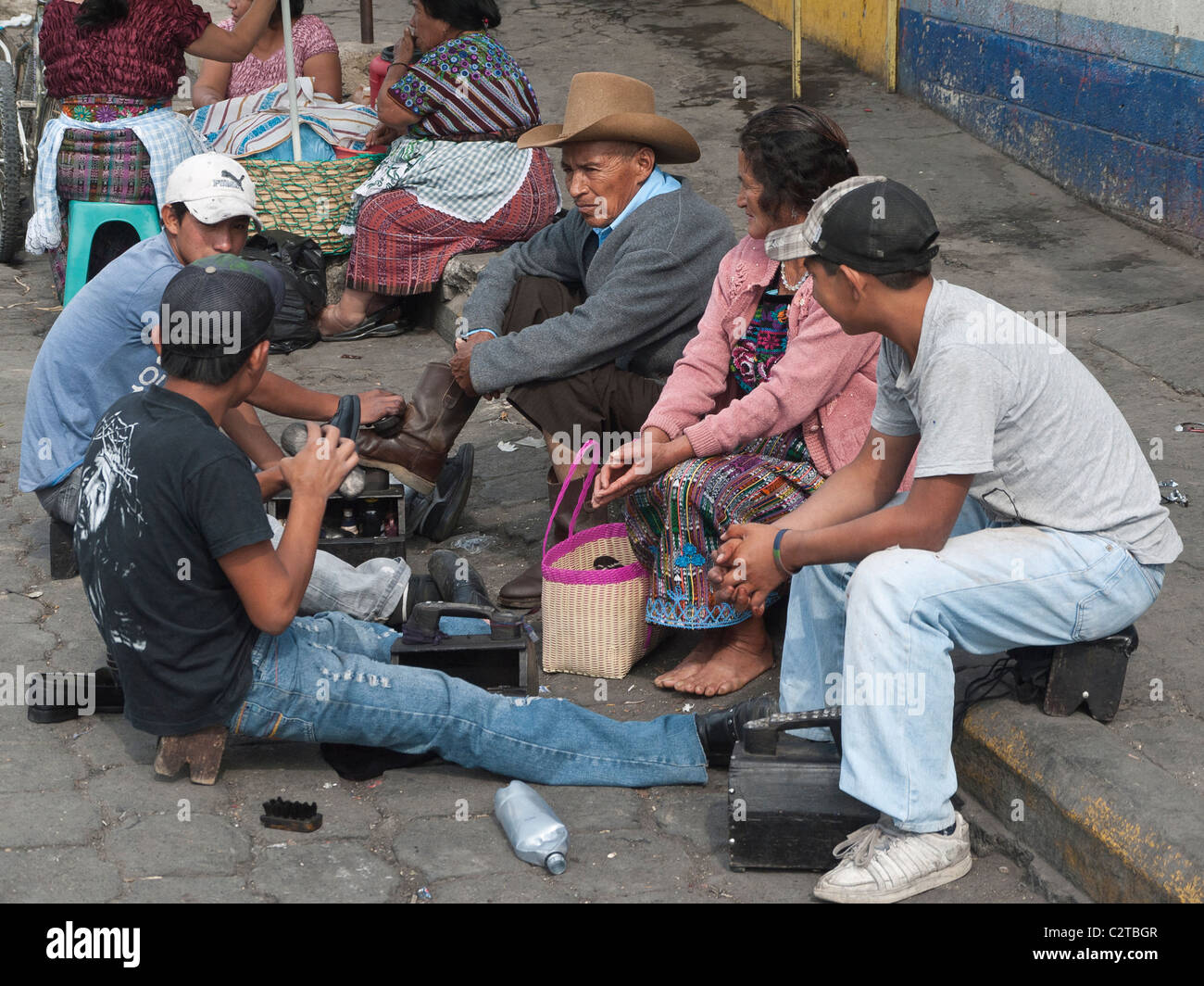 An older man has his shoes shined on the sidewalk while his wife looks on in Antigua, Guatemala. Stock Photo