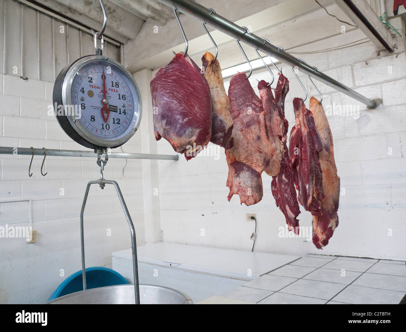 Fresh raw meat hangs from hooks in a butcher's stall at the public market in the Spanish colonial city of Antigua, Guatemala. Stock Photo