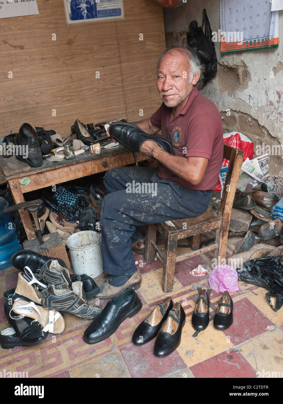 A cobbler works repairing a shoe in his shop on a side street in the city center in the Spanish colonial city of Antigua. Stock Photo