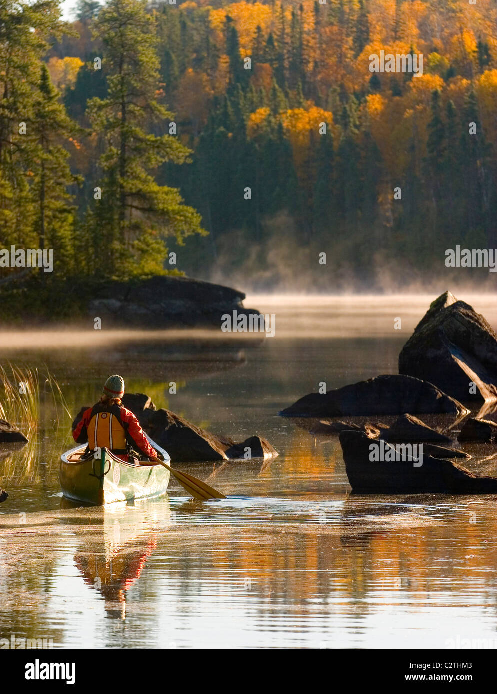 Woman paddles a canoe on a  lake in the early  morning in Autumn Boundary Waters in Superior National Forest Minnesota Stock Photo