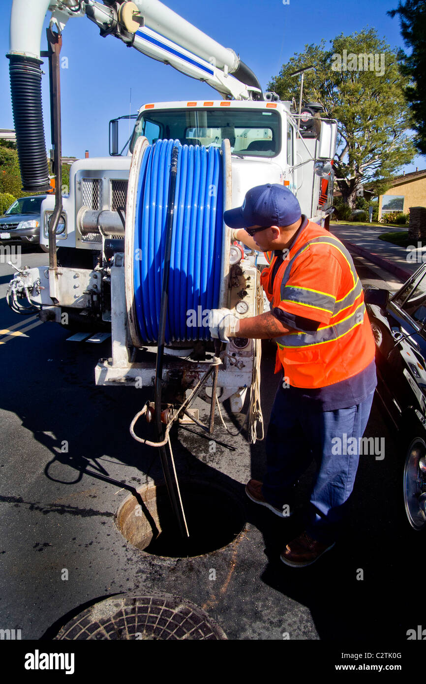 Using a truck mounted suction system, a technician cleans a clogged sewer in Laguna Niguel, CA. Note high visibility safety vest Stock Photo