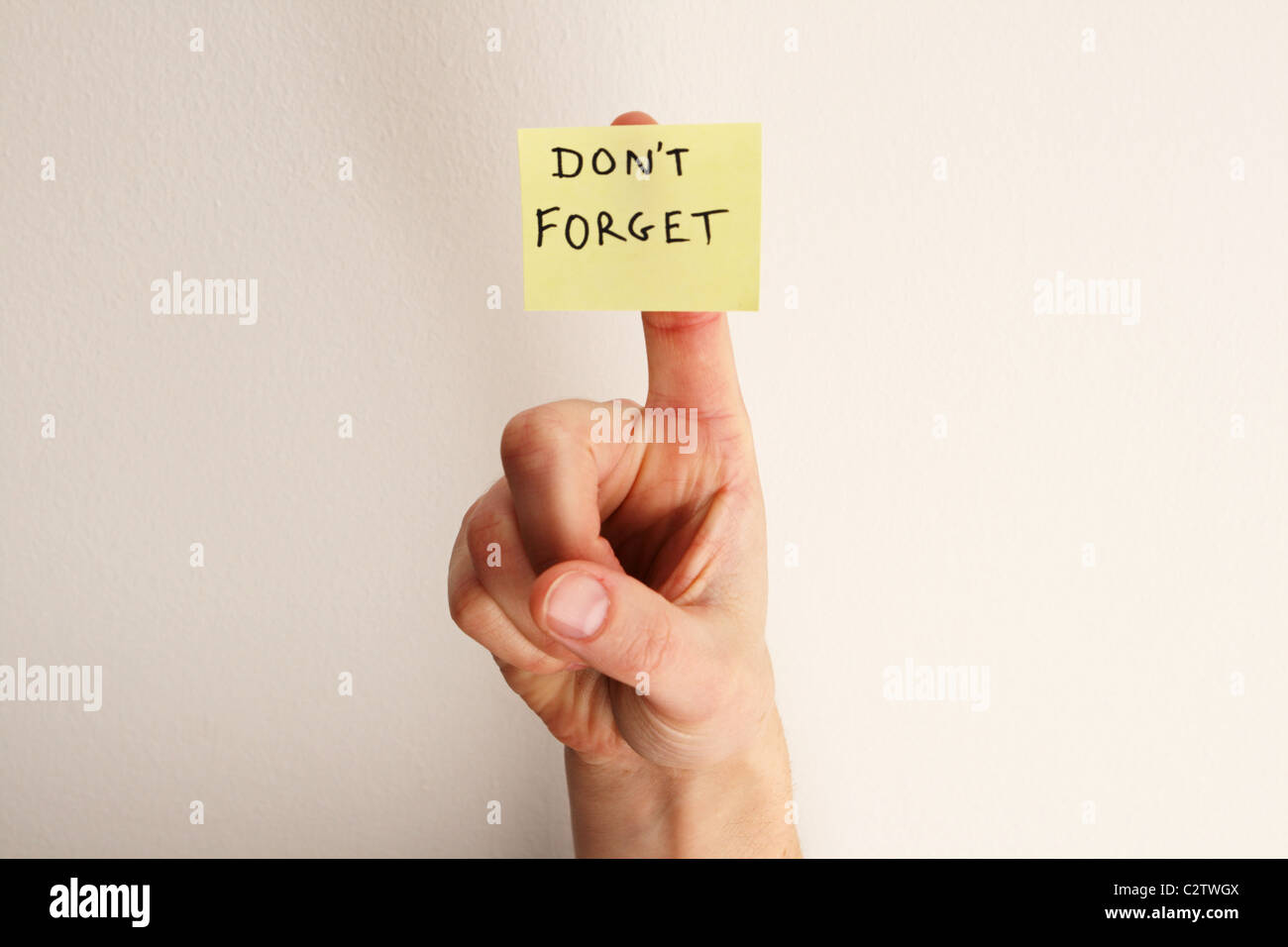 yellow sticky note saying don't forget on a woman's finger with off-white wall background Stock Photo