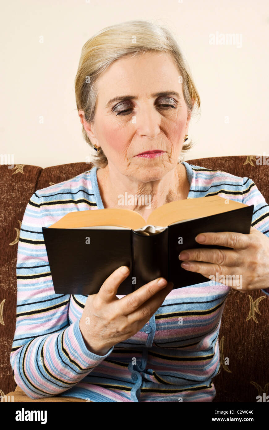 Older woman sitting in her couch and reading a book Stock Photo - Alamy