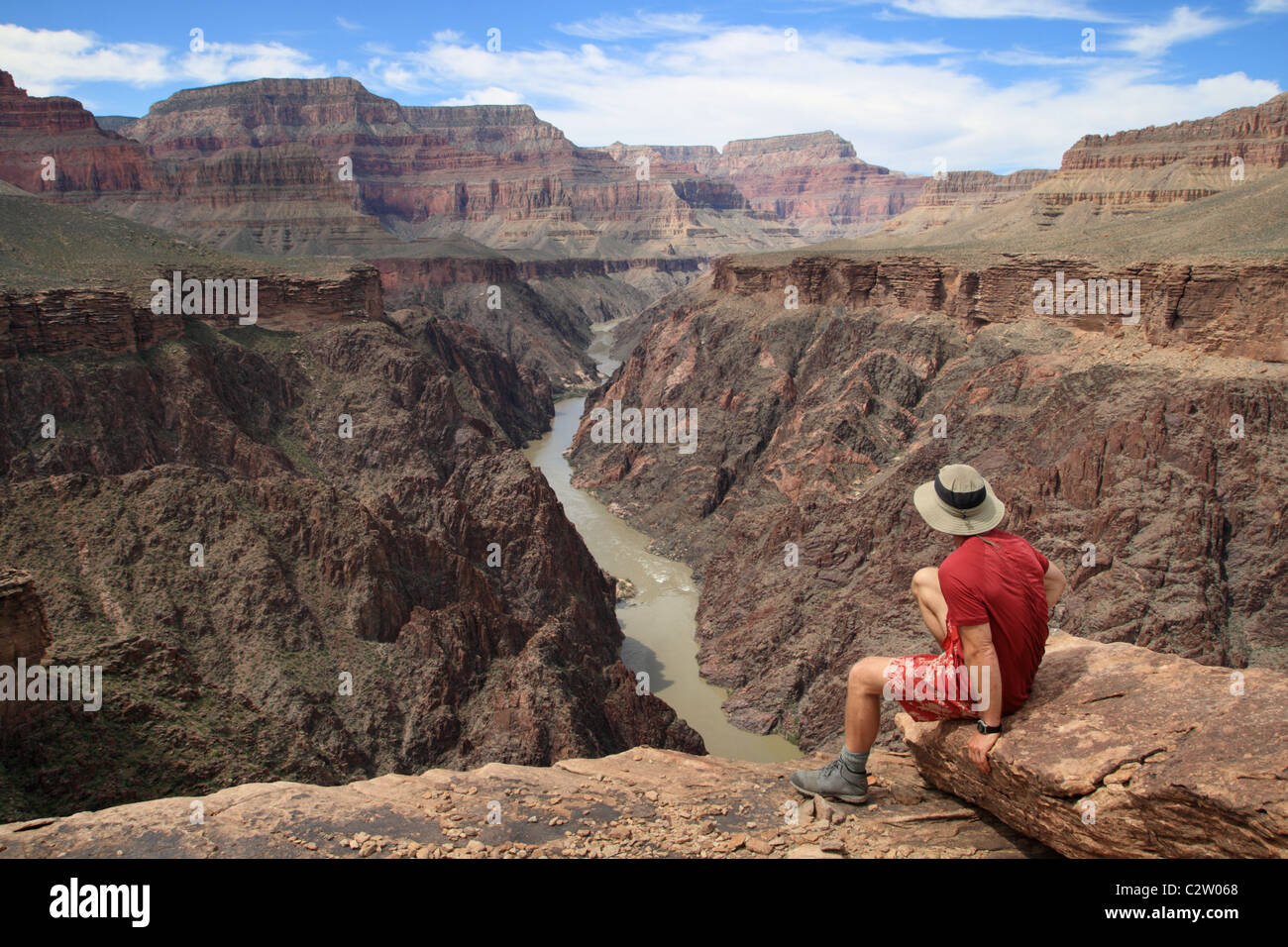 a man sitting on an overlook in the Grand Canyon looking down into Granite Gorge from the Tonto Plateau Stock Photo