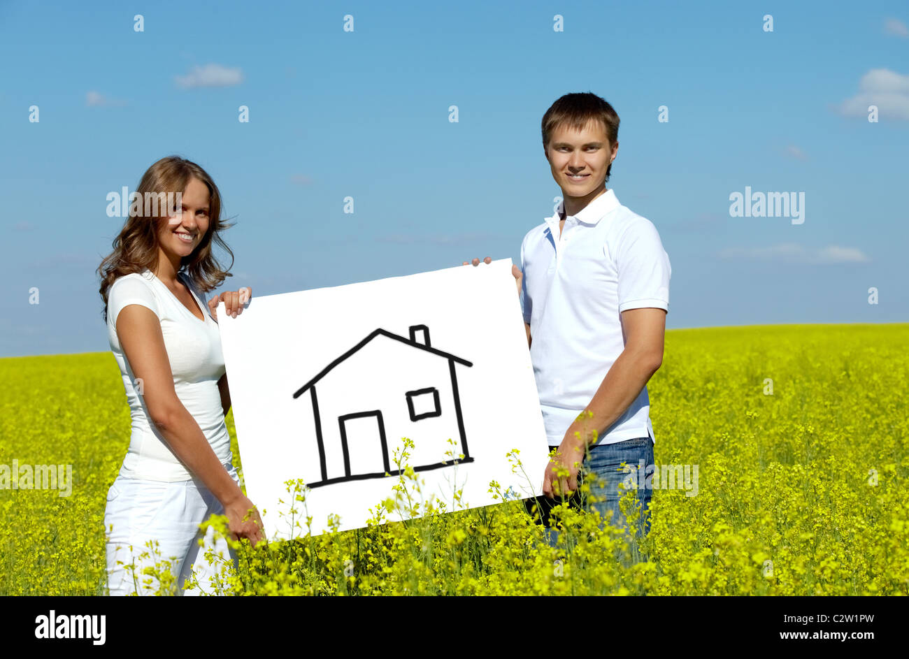 Portrait of happy young couple showing house drwan on paper in meadow Stock Photo