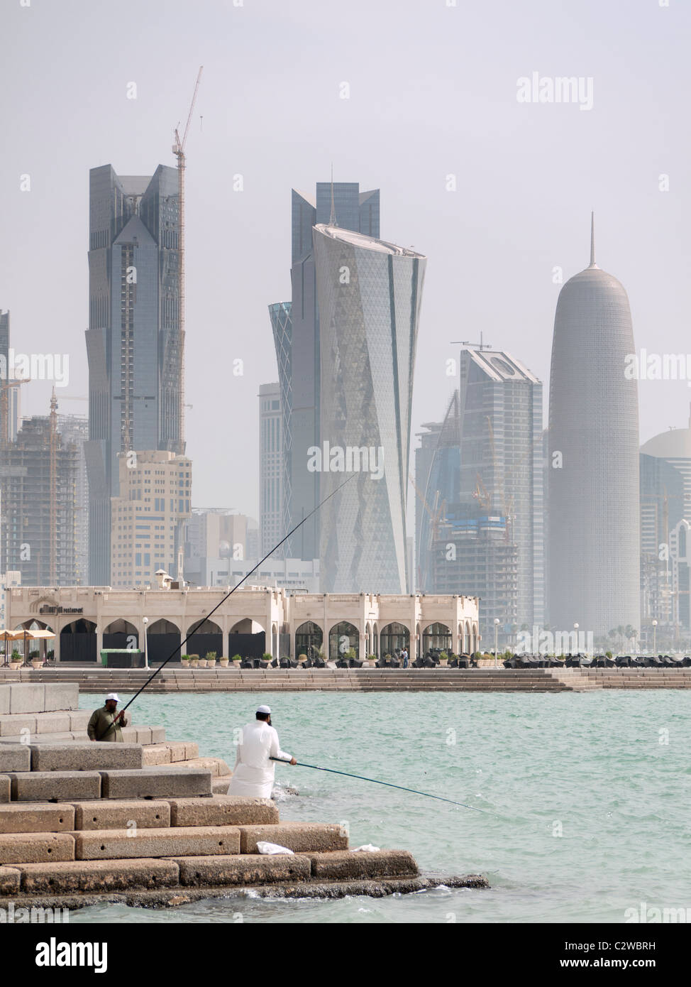 Men fishing on The Corniche with modern office towers and skyline in business district in Doha Qatar Stock Photo