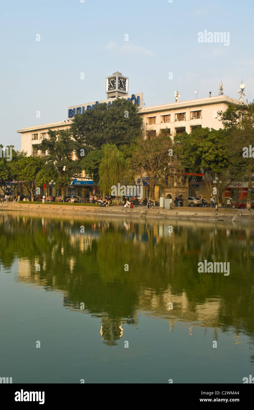 Vertical view of Hanoi's central Post Office reflected in Hoan Kiem Lake (Hồ Hoàn Kiếm) on a sunny evening. Stock Photo