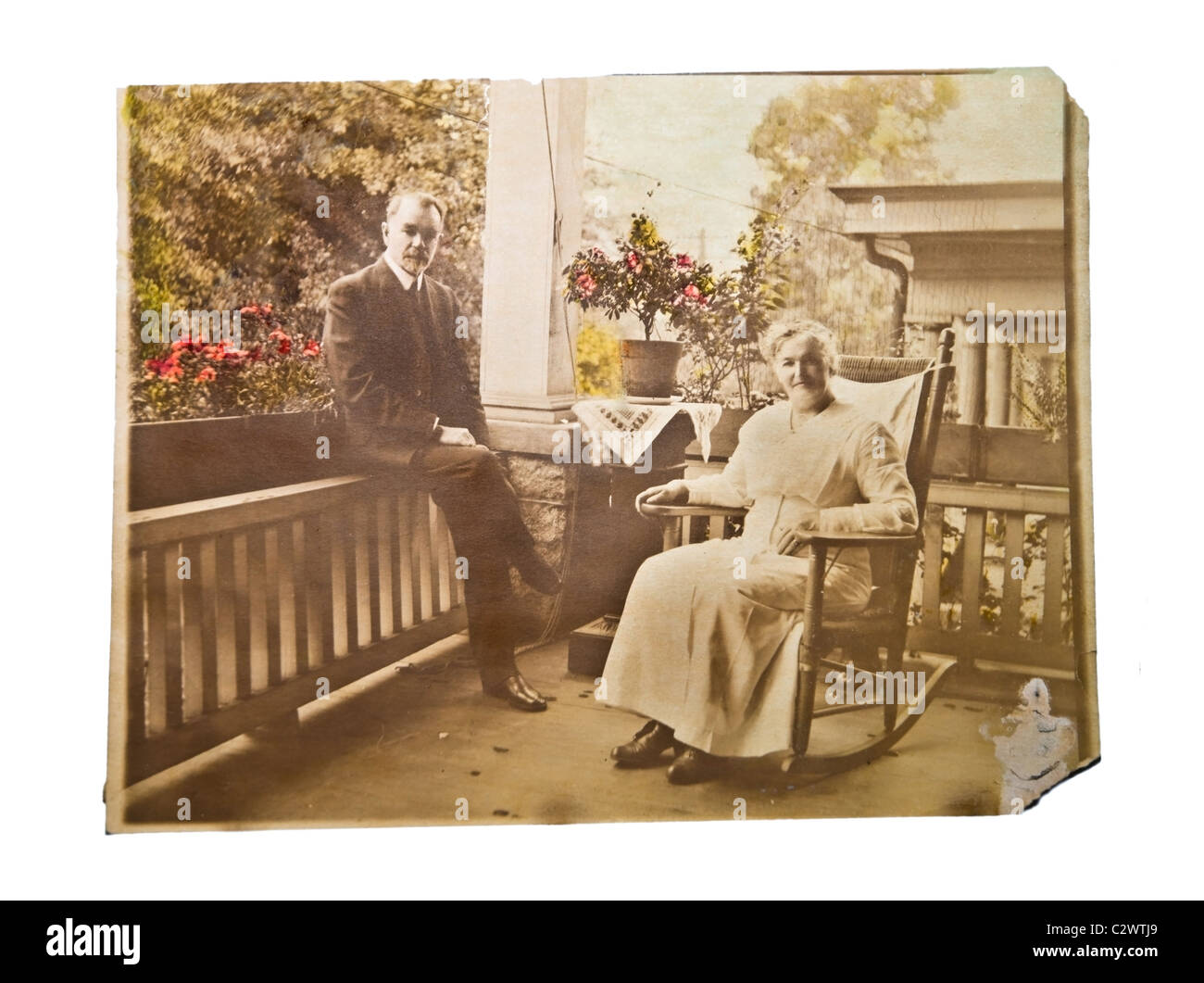 A vintage photograph of an older couple sitting on the porch of their home. It's sepia with some parts colorized. Stock Photo