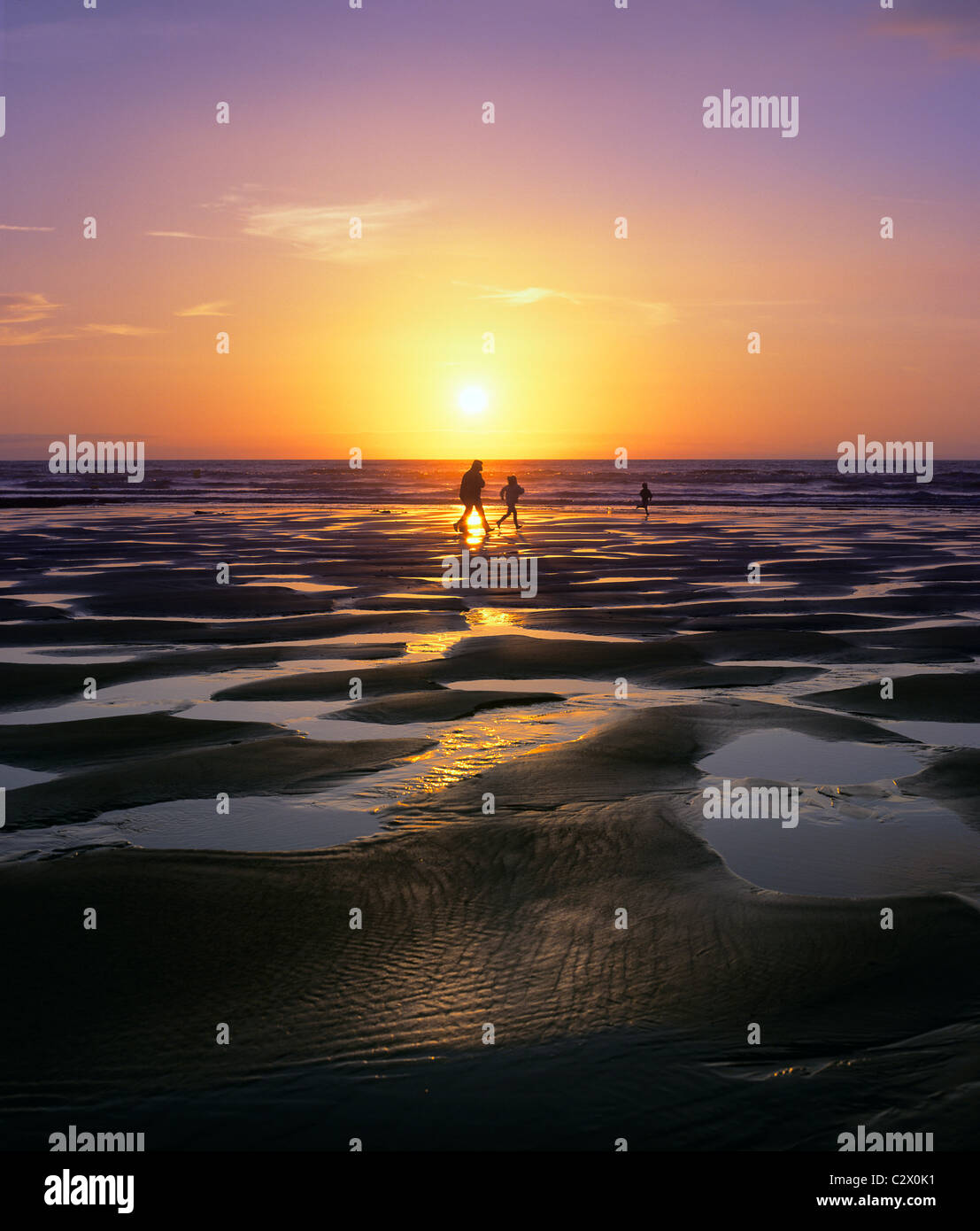 Adult, kids and setting sun over foreshore (area between high and low tide), Seaford, East Sussex. Stock Photo