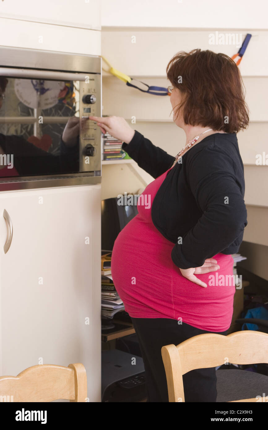 Pregnant Plus Sized Woman Standing In Kitchen Using Microwave Oven Stock Photo Alamy