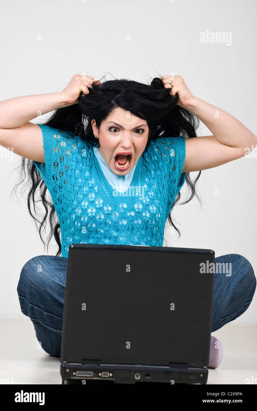 Angry woman pulling and tearing out her hair and screaming in front of laptop because of computer crashed ,data loss Stock Photo