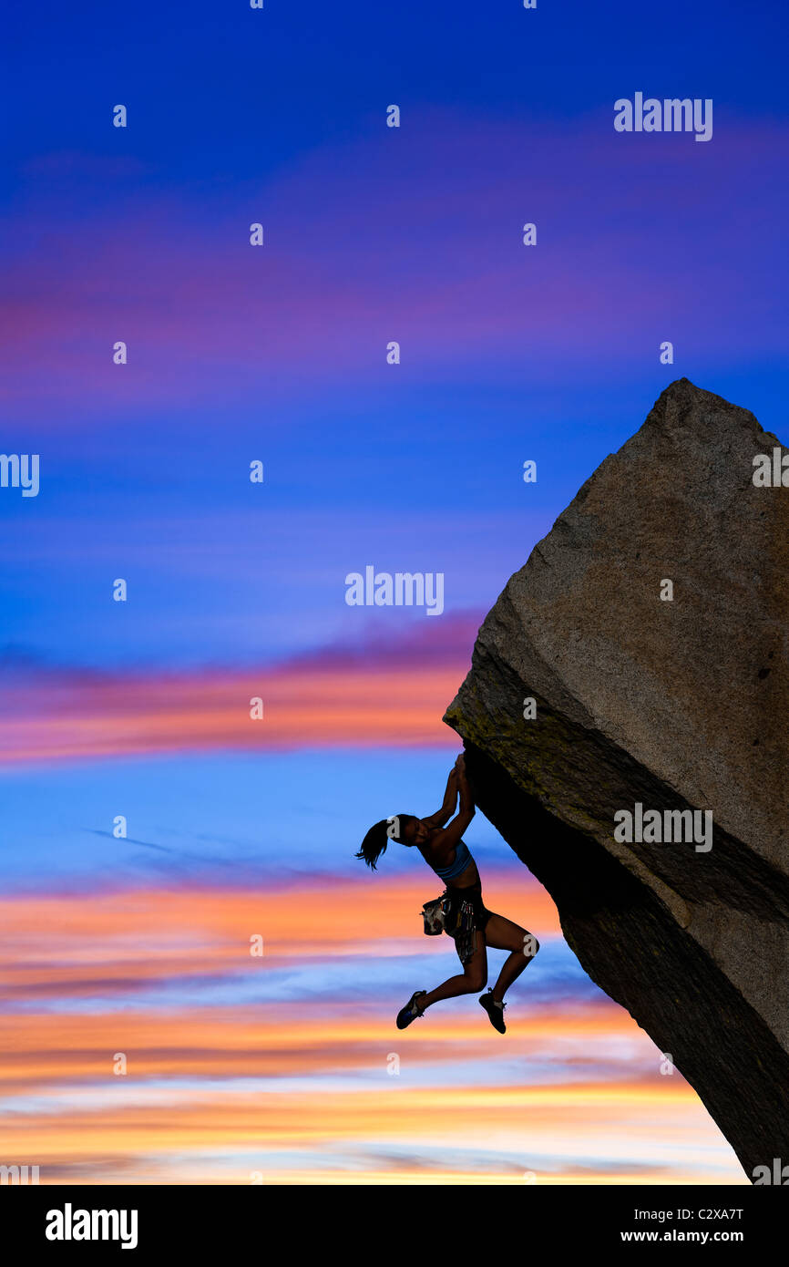 Female rock climber struggles to reach her next grip as she battles her way up a challenging cliff. Stock Photo