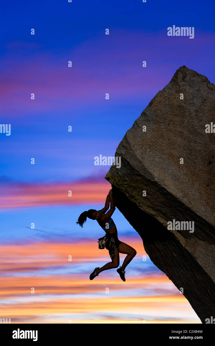 Female rock climber struggles to reach her next grip as she battles her way up a steep cliff. Stock Photo