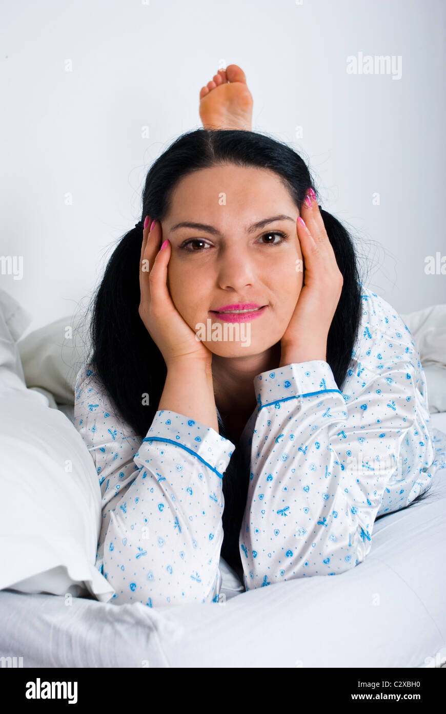 https://c8.alamy.com/comp/C2XBH0/happy-woman-laying-on-bed-with-legs-up-and-holding-hands-on-face-C2XBH0.jpg