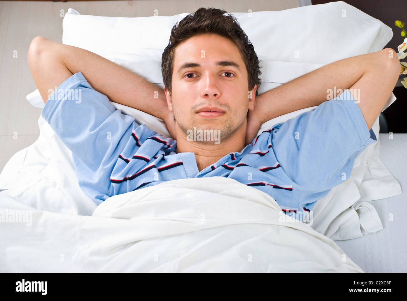 Young man lying on bed with hands under head and relaxing Stock Photo