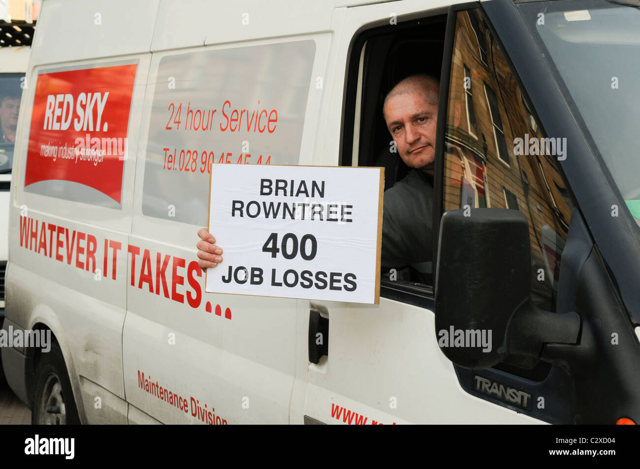 Belfast, Northern Ireland. 20 Apr 2011 - Employee from contracting firm Red Sky holds a protest banner saying 'Brian rowntree [NIHE Chairman] 400 Job Losses' while he drives past NIHE HQ over cancellation of their contract to maintain Housing executive stock Stock Photo