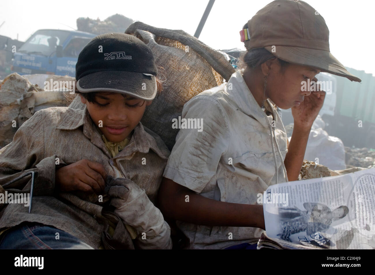 Two child laborer girls are taking a break from their jobs at a polluted garbage dump in Cambodia. Stock Photo