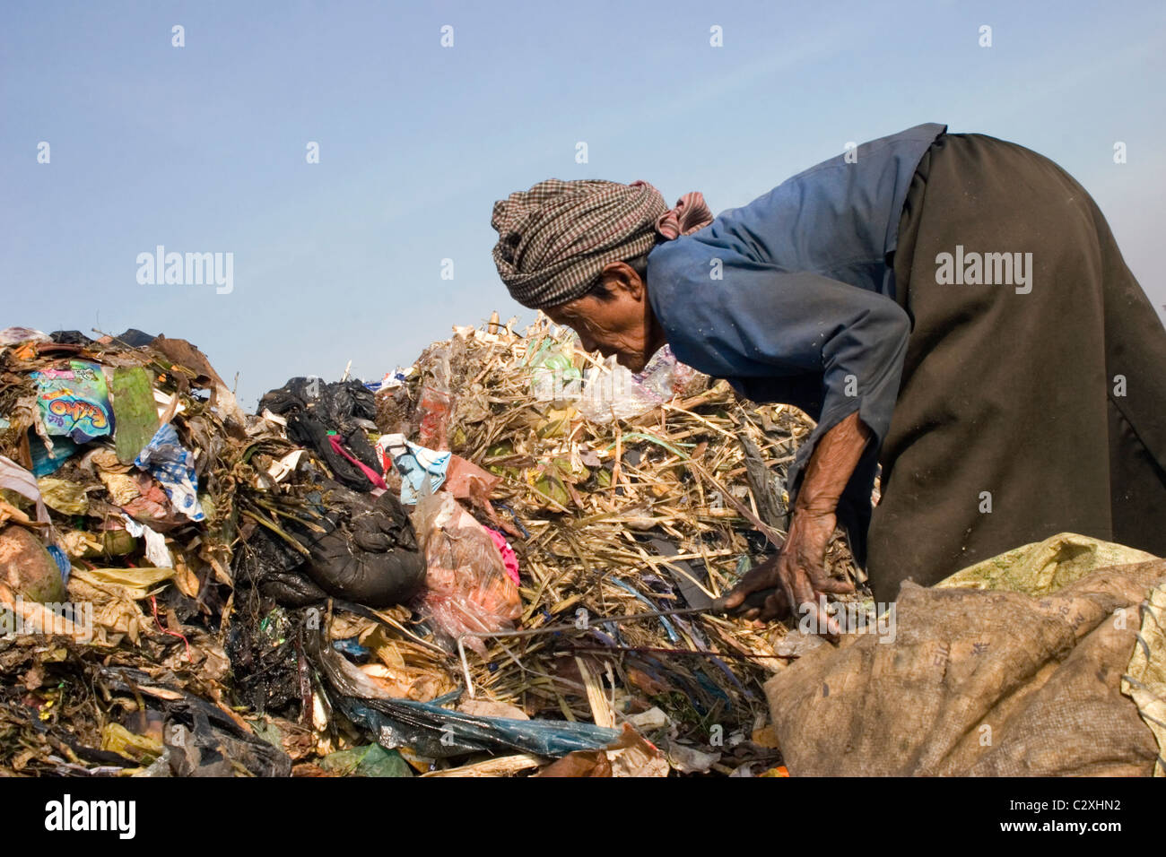 An elderly woman is searching for recyclable material at a polluted garbage dump in Cambodia. Stock Photo
