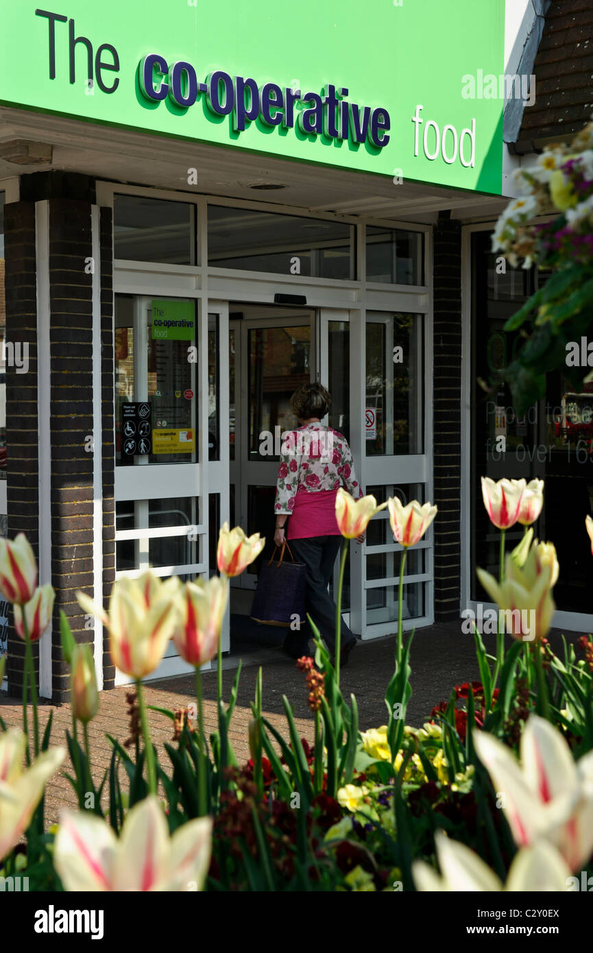 A woman enters the Co-Operative food shop with flowers in the foreground, Rustington, Littlehampton, West Sussex. Stock Photo
