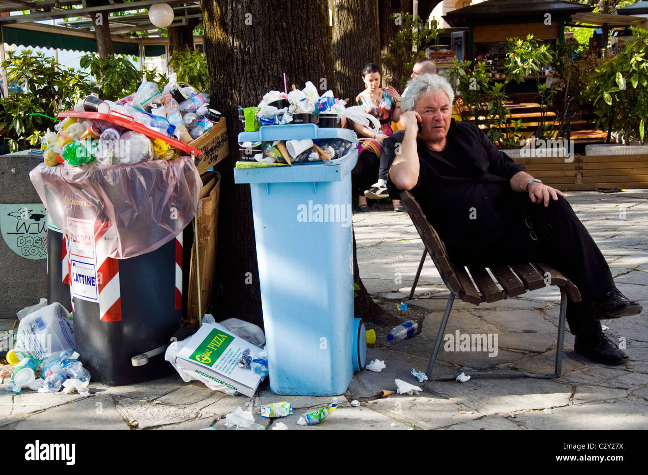 A man sits by overflowing rubbish bins on Isola Bella Stock Photo