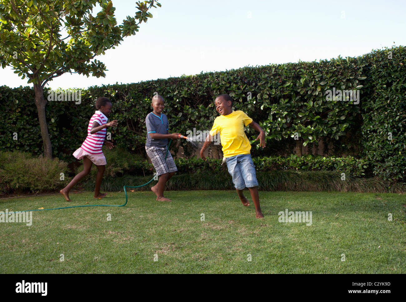 Children chasing each other with water hose, Johannesburg, South Africa Stock Photo
