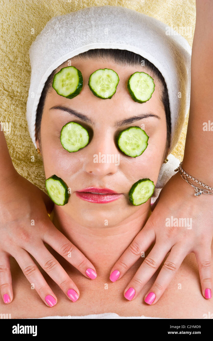 Young woman with cucumber mask getting a neck massage from a masseuse at spa salon Stock Photo