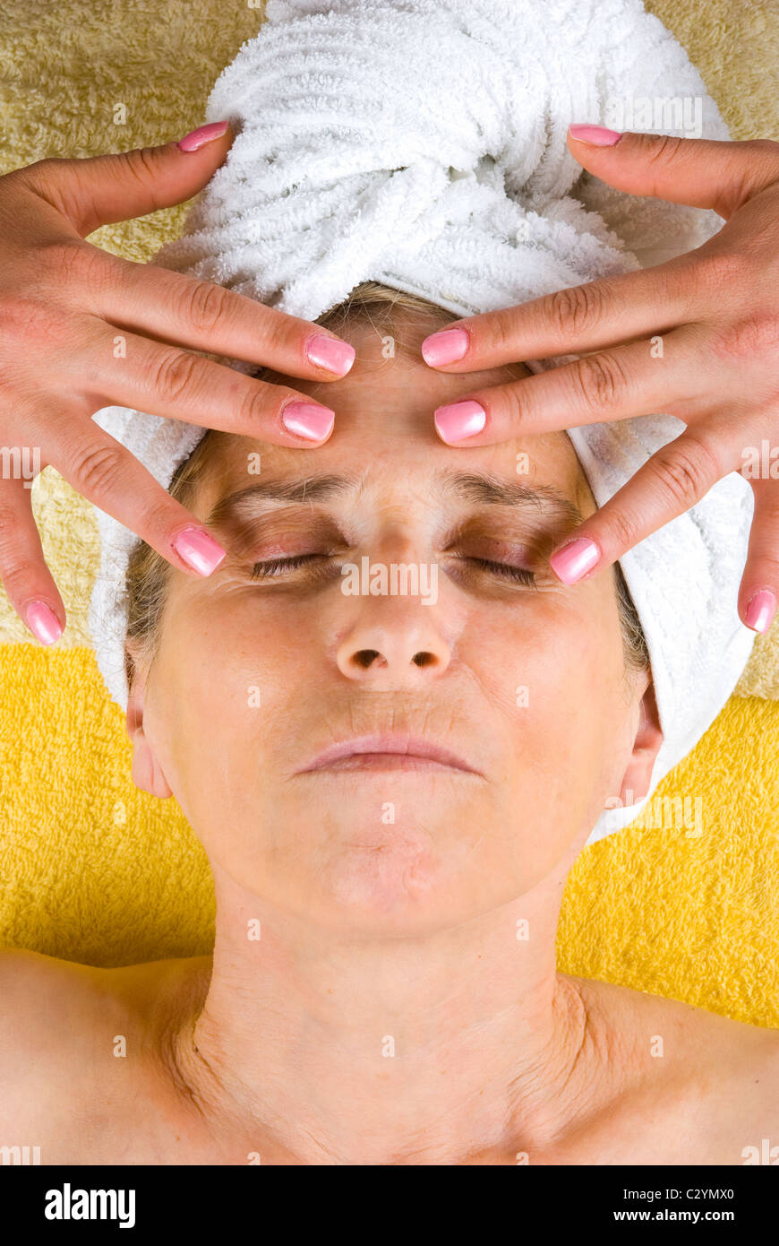 Senior woman lying with eyes closed and receiving a facial massage at spa resort Stock Photo