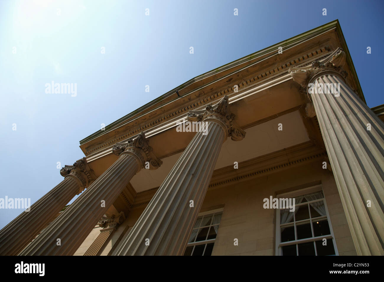 Looking up at building with 4 Grecian Columns windows and blue sky with sun Stock Photo