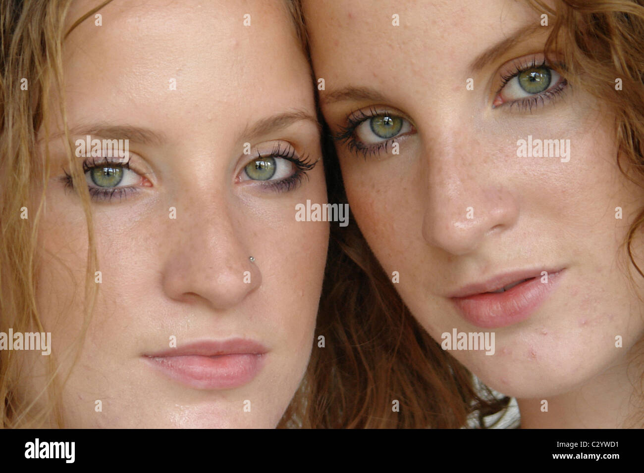Closeup Portrait of Twin Sisters with Serious Expression Posing Cheek to Cheek Stock Photo